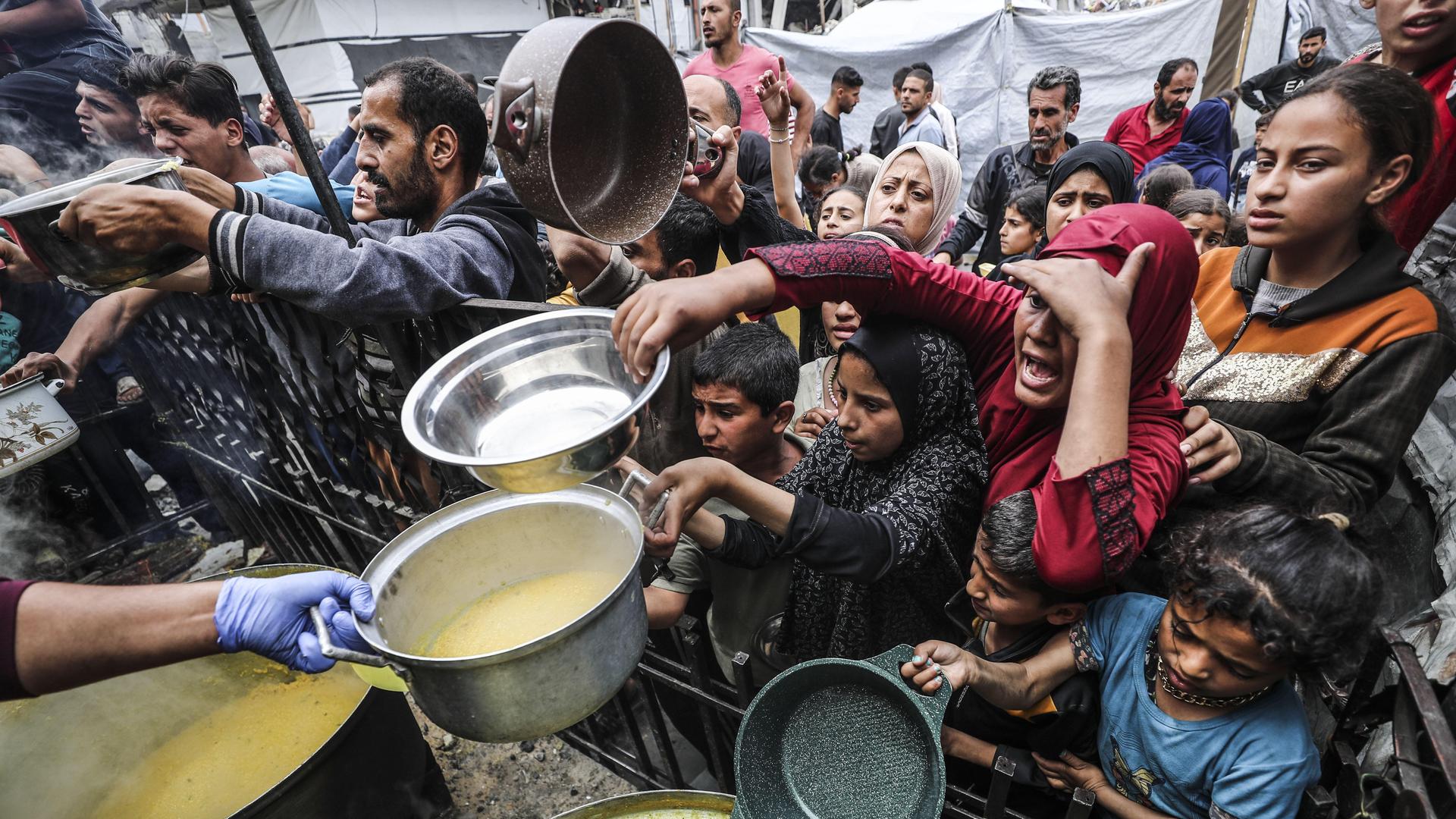 Männer, Frauen und Kinder drängen sich mit ausgestreckten Händen und Containern, um warme Mahlzeiten zu erhalten, die von Hilfsorganisationen verteilt werden.