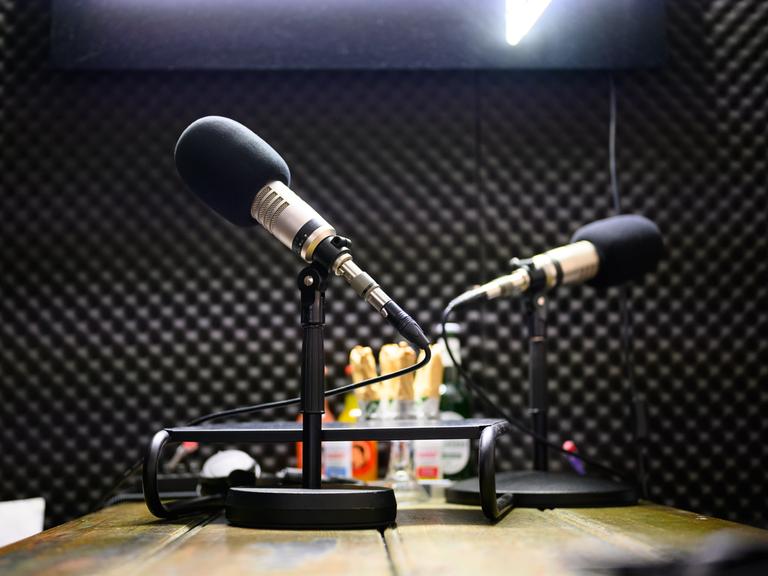 Zwei Podcast-Mikrofone stehen in einem Tonstudio auf einem Tisch.