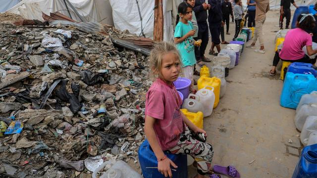 Am Rande eines Trümmerfeldes warten Kinder in Gaza mit bunten Plastikkanistern auf die Ausgabe von frischem Trinkwasser.