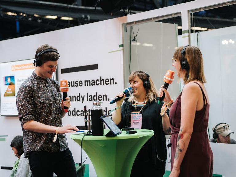 Auf einer Bühne in einer Messehalle stehen Mike Herbstreuth, Maria Lorenz-Bokelberg und Carina Schroeder in gelöster Gesprächshaltung.