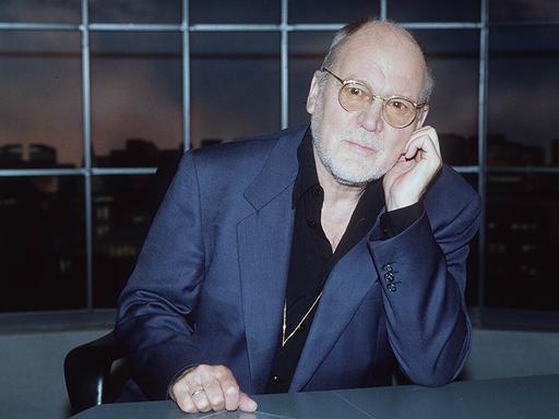 Hanns Dieter Hüsch 1995 aufgenommen, er sitzt an einem Tisch und schaut in die Kamera