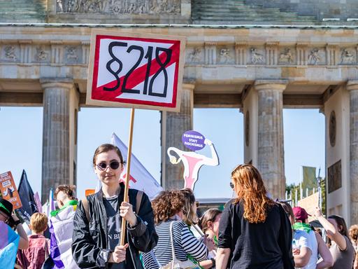 Eine junge Demonstrantin hält während eines Protest vor dem Brandenburger Tor ein Schild mit der durchgestrichenen Aufschrift "§ 218" in die Höhe.