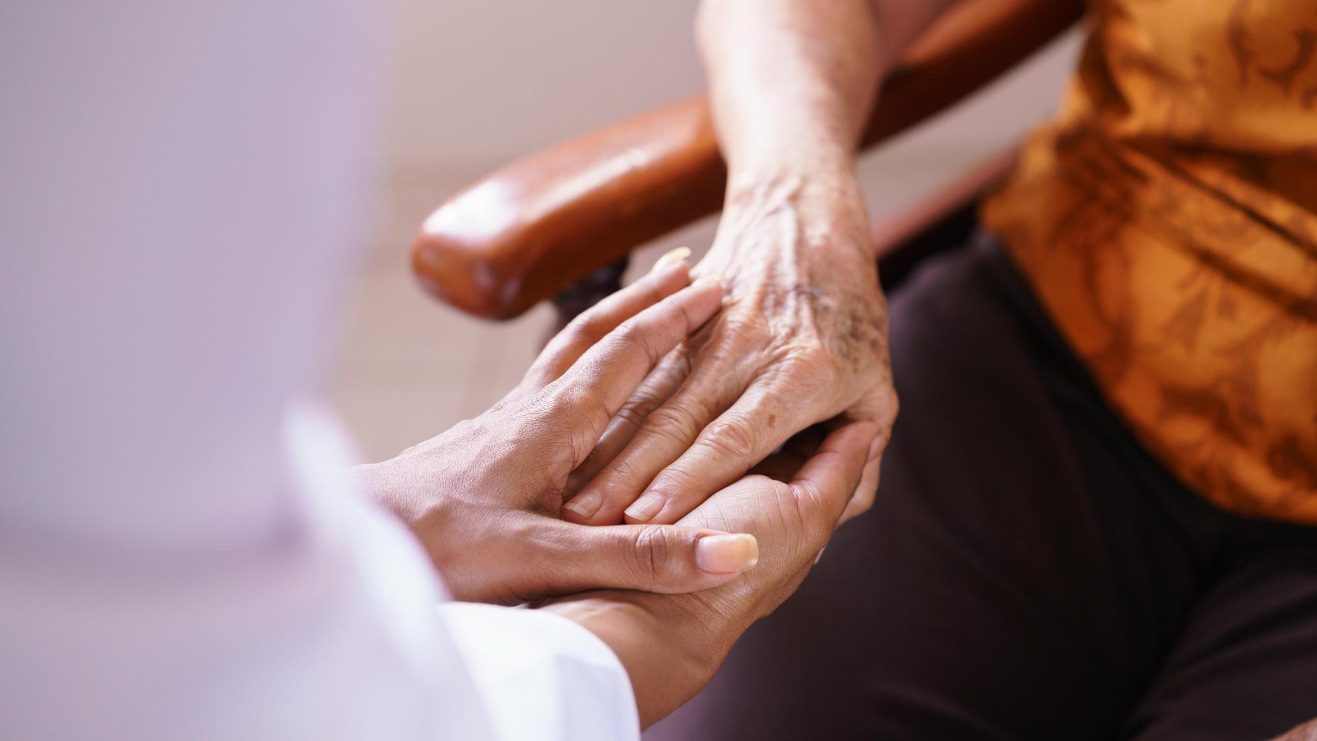Eine Pflegerin hält die Hände einer alten Patientin in der Hand