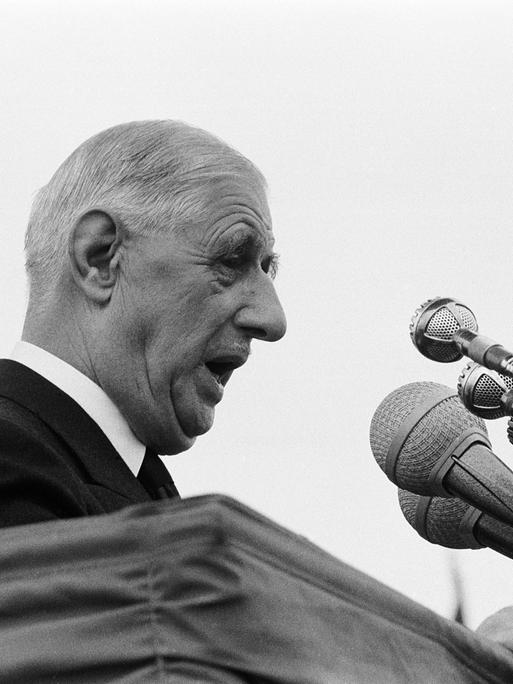 Der französische Staatspräsident Charles de Gaulle steht vor Mikrofonen an einem Pult und hält eine Rede.