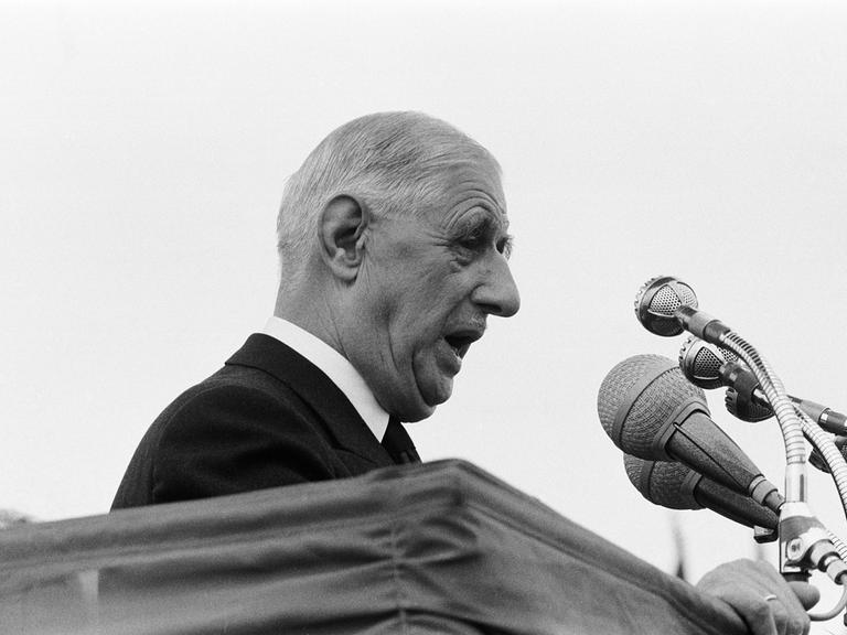 Der französische Staatspräsident Charles de Gaulle steht vor Mikrofonen an einem Pult und hält eine Rede.