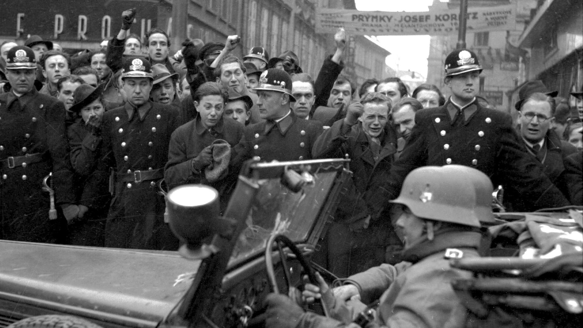 Einheiten der deutschen Wehrmacht ziehen am 15. März 1939 in Prag ein. Am Straßenrand stehen Einwohner der Stadt, die den Einmarsch mit geballten Fäusten quittieren.