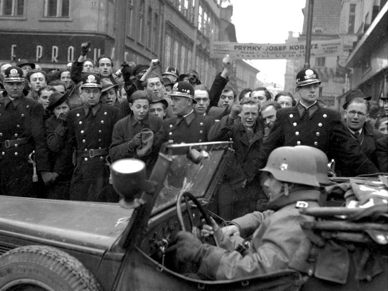 Einheiten der deutschen Wehrmacht ziehen am 15. März 1939 in Prag ein. Am Straßenrand stehen Einwohner der Stadt, die den Einmarsch mit geballten Fäusten quittieren.
