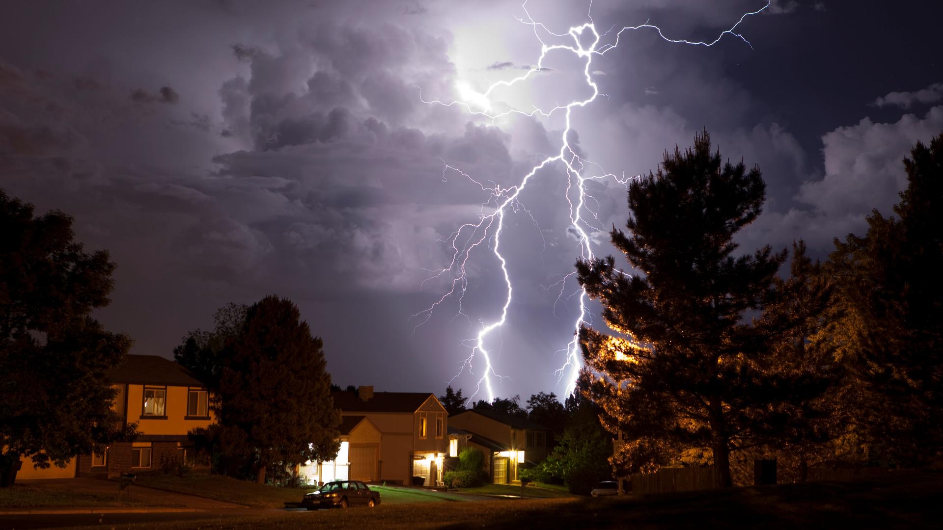 Über einem Wohngebiet steht eine Gewitterwolke, aus der ein weit verzweigter Blitz hervorschlägt. Über einem Wohngebiet steht eine Gewitterwolke, aus der ein weit verzweigter Blitz hervorschlägt.
