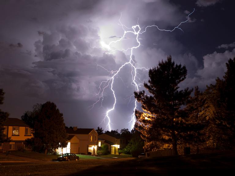 Über einem Wohngebiet steht eine Gewitterwolke, aus der ein weit verzweigter Blitz hervorschlägt.