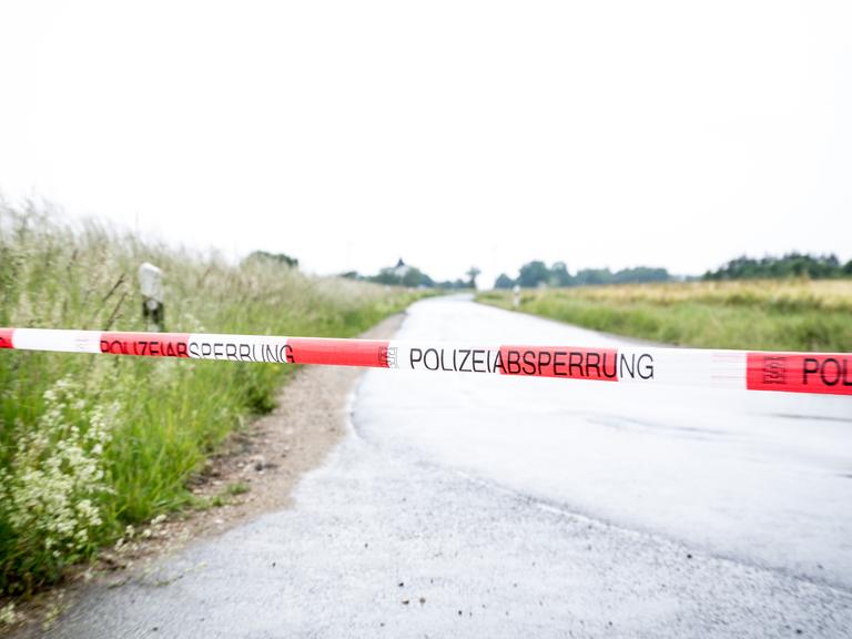 Ein rot-weiß gestreiftes Polizeiband ist quer über eine Landstraße gespannt.