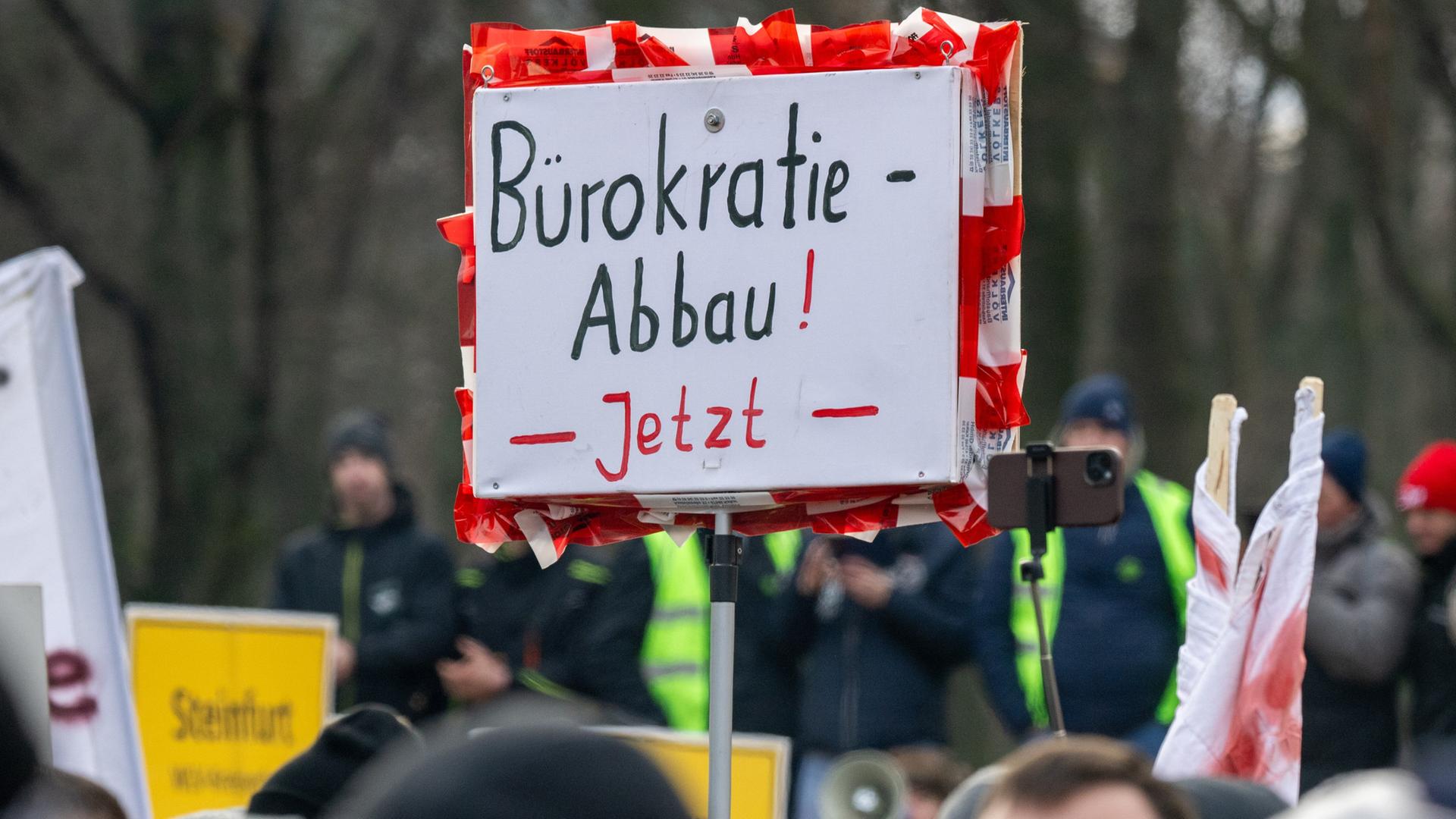 Bei einer Kundgebung hält jemand ein Schild mit der Aufschrift „Bürokratie-Abbau! Jetzt“ hoch.