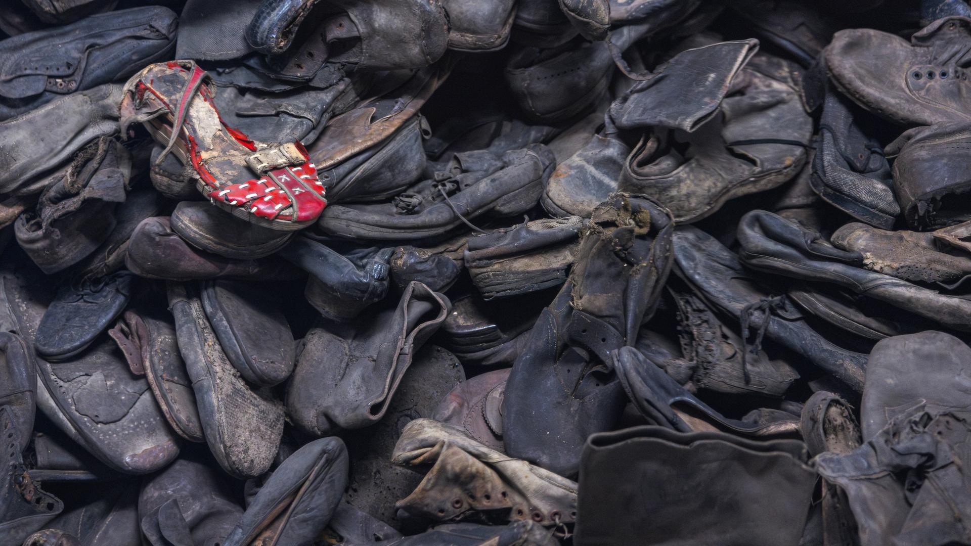 Unzählige dunkle Schuhe auf einem Haufen, ein roter Schuh liegt oben drauf. Es sind Schuhe in der Gedenkstätte Auschwitz-Birkenau. Unzählige dunkle Schuhe auf einem Haufen, ein roter Schuh liegt oben drauf. Es sind Schuhe in der Gedenkstätte Auschwitz-Birkenau.