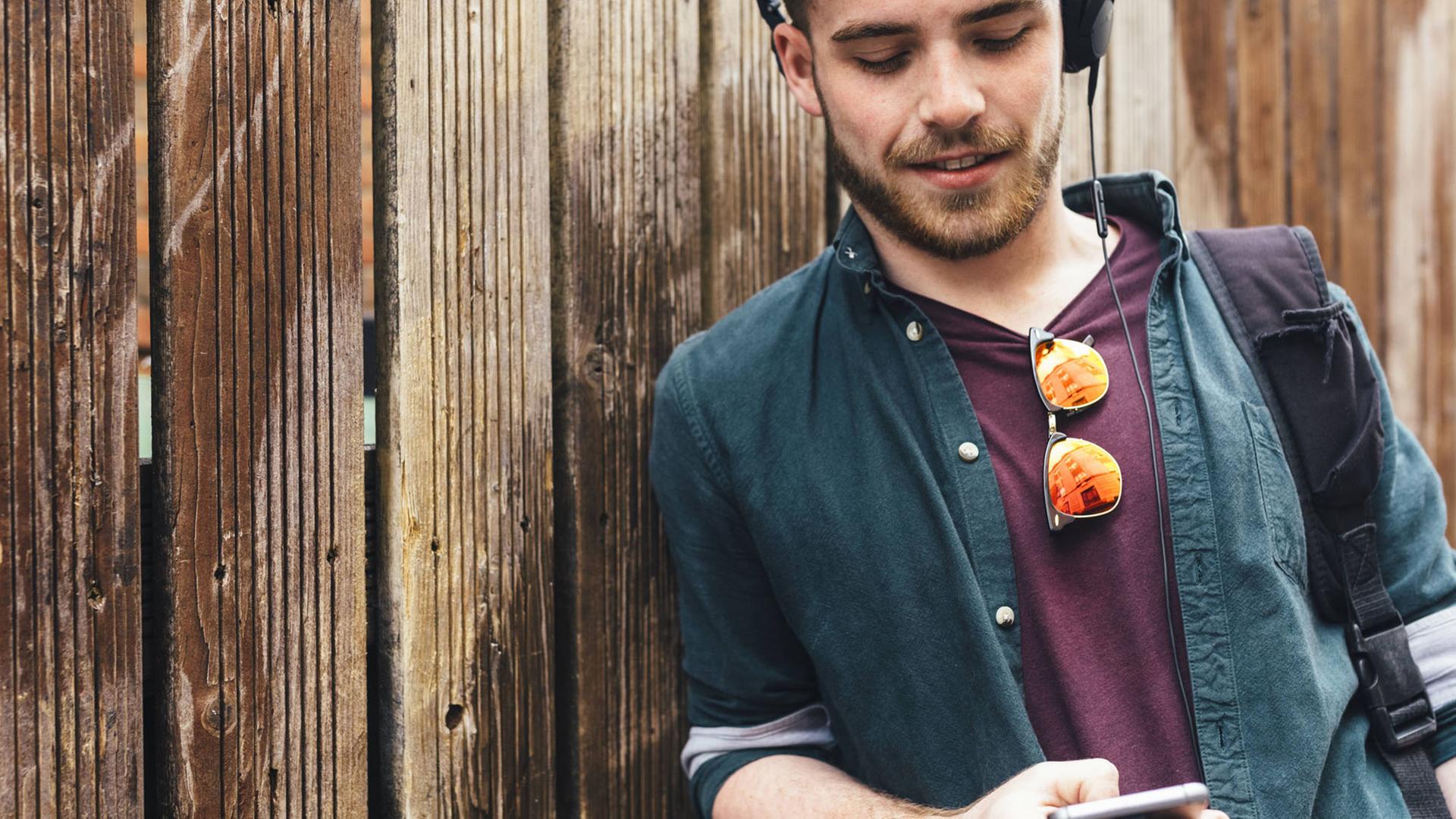 Ein junger Mann mit Kopfhörern scrollt auf seinem Smartphone.