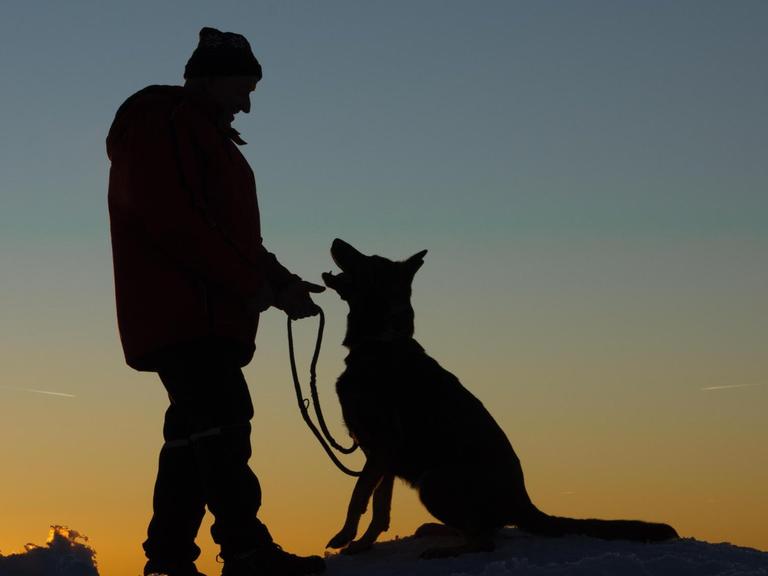 Ein Mann mit Hund im Schnee bei Sonnenuntergang.