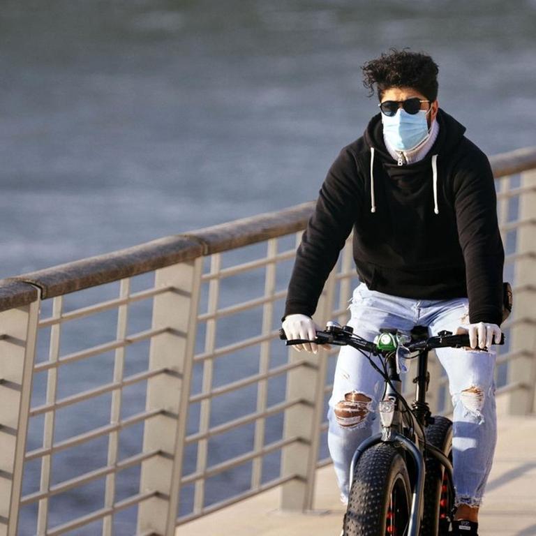 Ein Radfahrer mit Atemschutzmasker am Rheinboulevard in Köln.