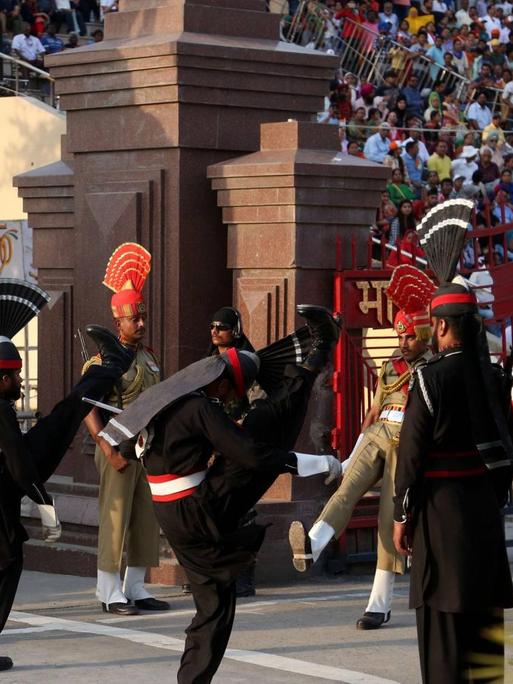 Pakistanische Soldaten in schwarzen Uniformen treffen auf indische Soldaten während einer Fahnenzeremonie am einzigen Grenzübergang in Wagah. Viele Zuschauer aus den verfeindeten Staaten verfolgen die "Beating retreat ceremony".