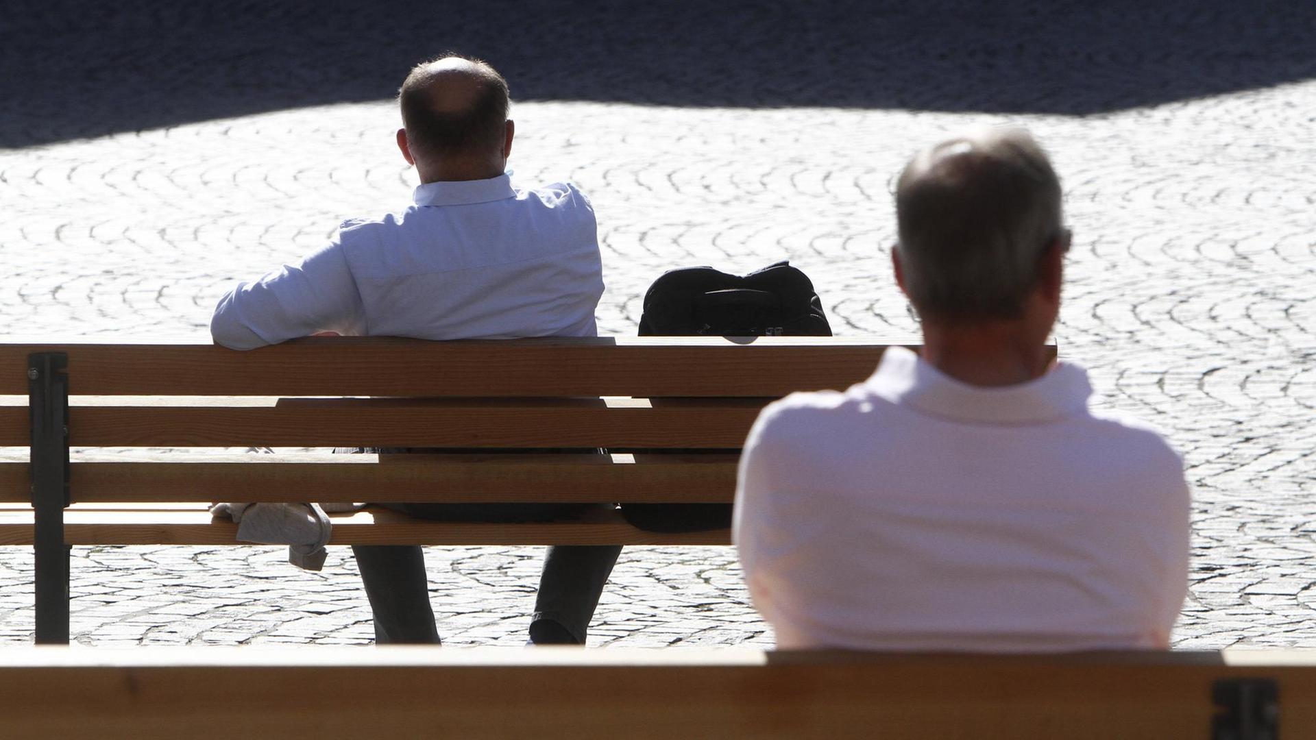 Zwei Männer sitzen einzeln auf zwei Bänken.