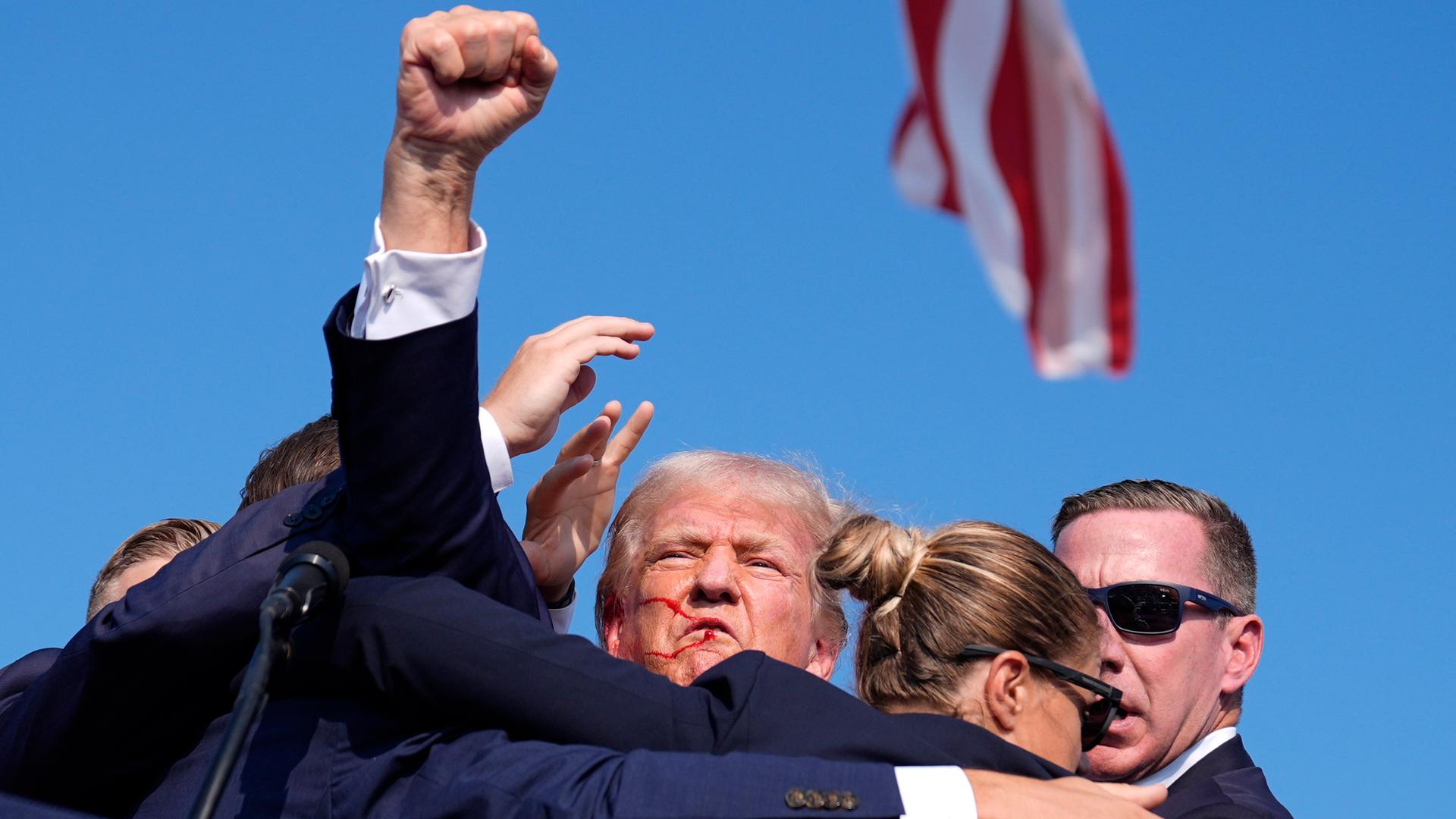 Donald Trump wird nach dem Attentat von Sicherheitskräften abgeschirmt und reckt die Faust in die Luft.