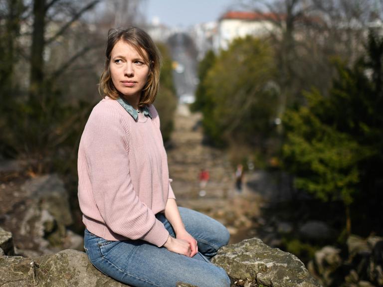 Anna Brüggemann sitzt in einem Park und blickt ernst ins Off des Bildes